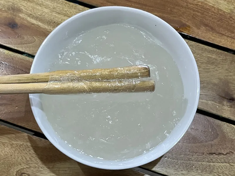 Papeda sagu yang sudah jadi di mangkuk putih, bening keabu-abuan dan kental menempel di sumpit