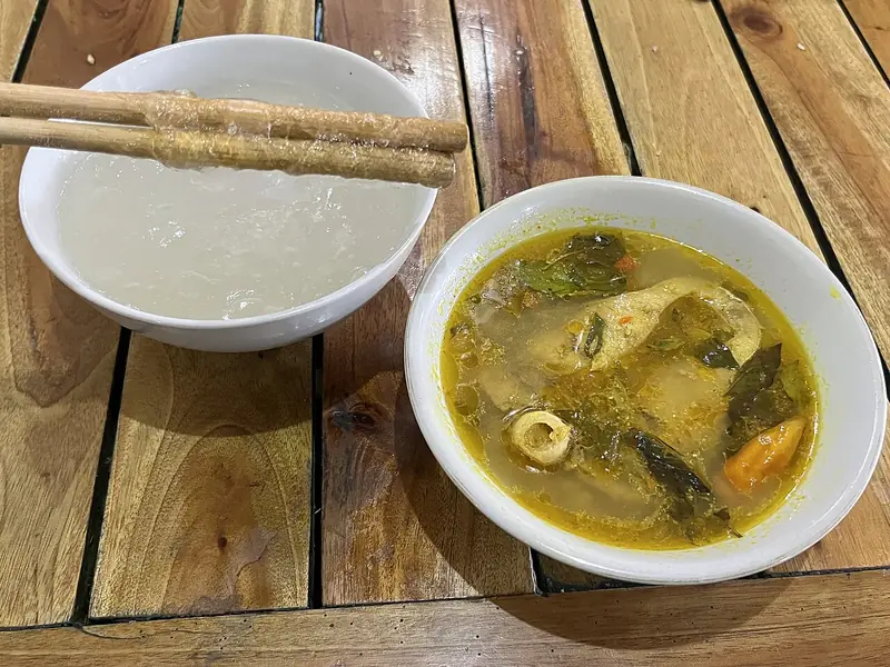 Semangkuk papeda dengan sumpit kayu di samping semangkuk ikan kuah kuning berisi daun kemangi