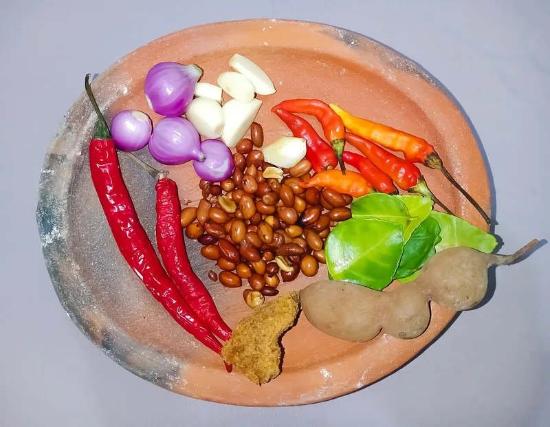 Bahan bumbu pecel di cobek tanah liat: kacang tanah, cabai, bawang merah, bawang putih, daun jeruk, asam jawa