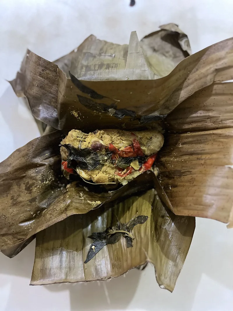 Pepes tahu yang baru dibuka dari daun pisang, tampak padat dengan cabai merah dan kemangi
