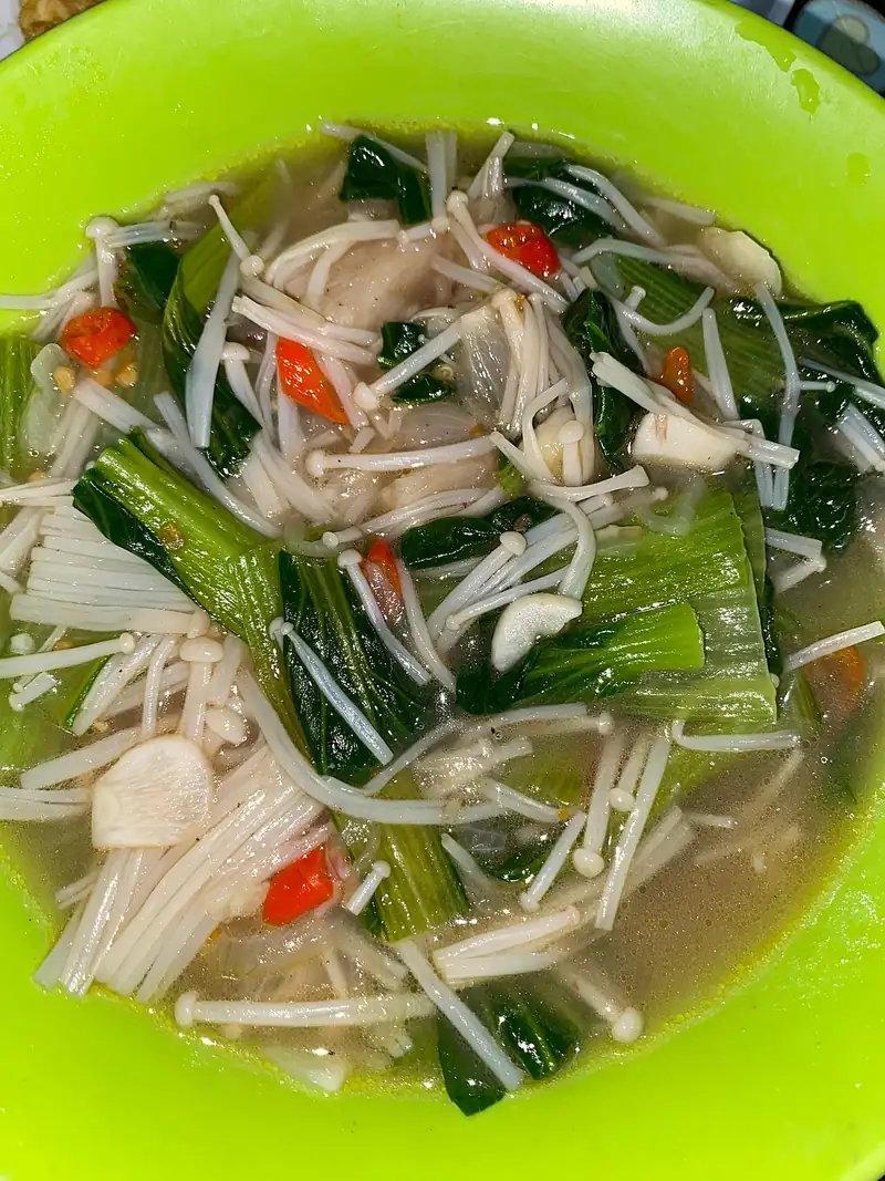 Tumis pokcoy berkuah dengan jamur enoki, irisan bawang putih, dan cabai merah di mangkuk hijau