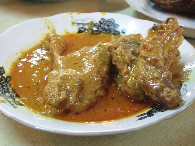 Beberapa potong gulai ayam dengan kuah santan kuning berminyak di piring putih bermotif hitam
