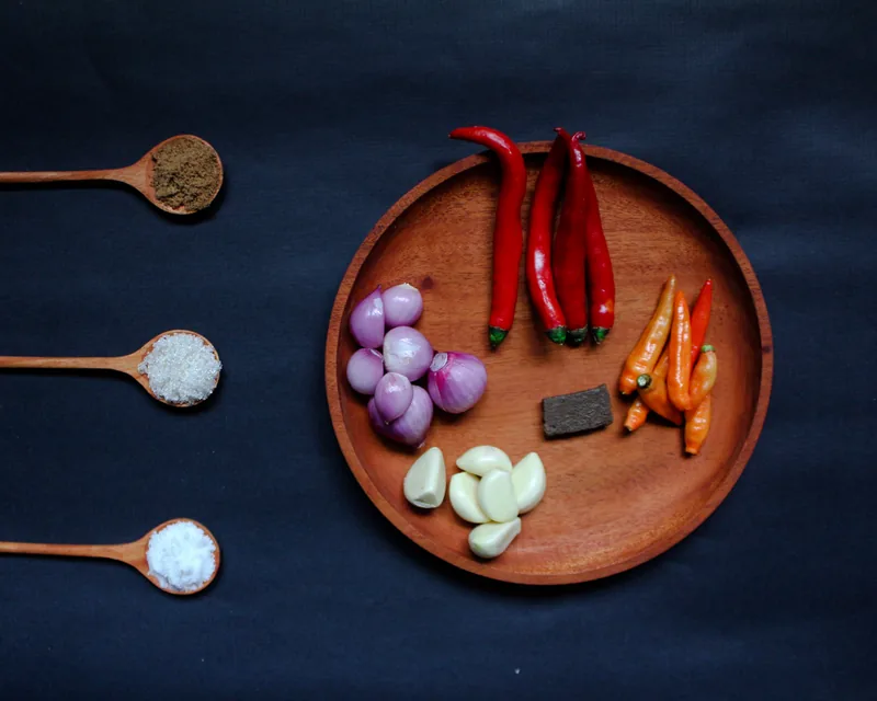 Bahan sambal bawang di piring kayu: cabai merah, cabai rawit, bawang merah, bawang putih, dan terasi