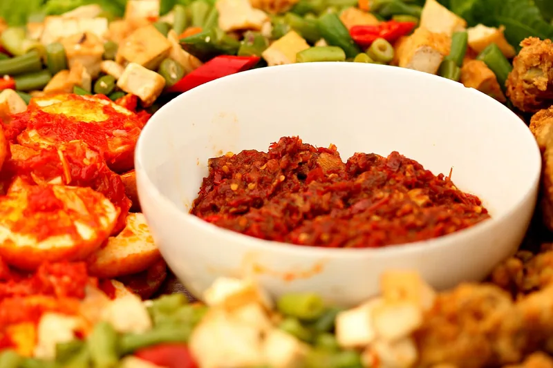 Semangkuk sambal merah disajikan di tengah lauk telur balado, gorengan, dan tumis buncis