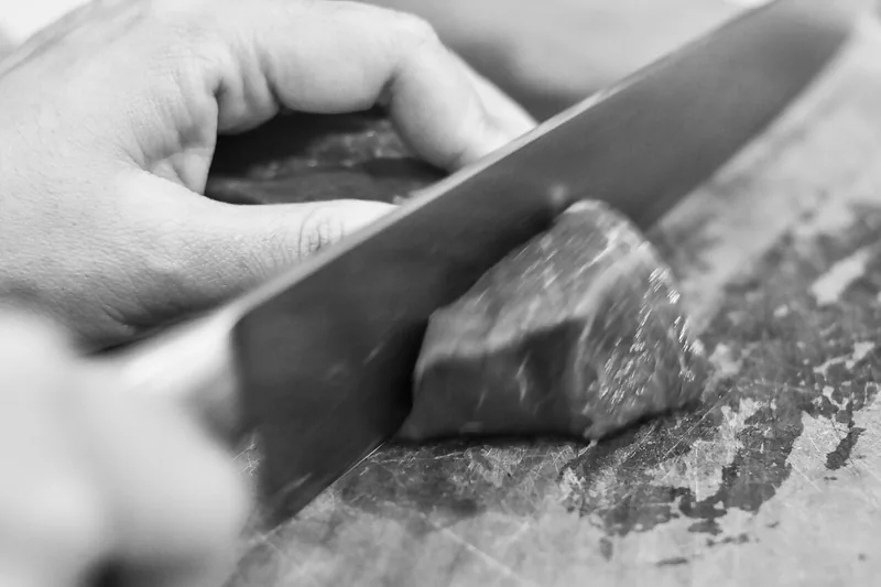 Tangan memotong bongkahan daging sapi mentah dengan pisau besar di atas talenan kayu