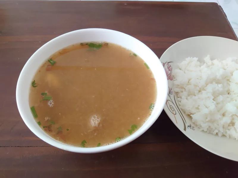 Semangkuk sop ayam bertabur irisan daun bawang disajikan dengan sepiring nasi putih