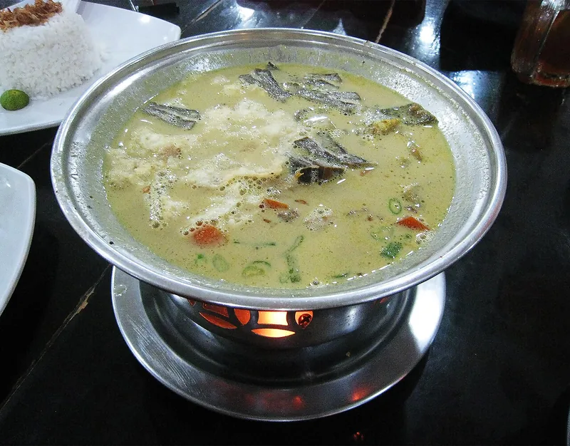 Kuah soto betawi santan kekuningan dengan daging dan wortel dalam panci kecil di atas tungku