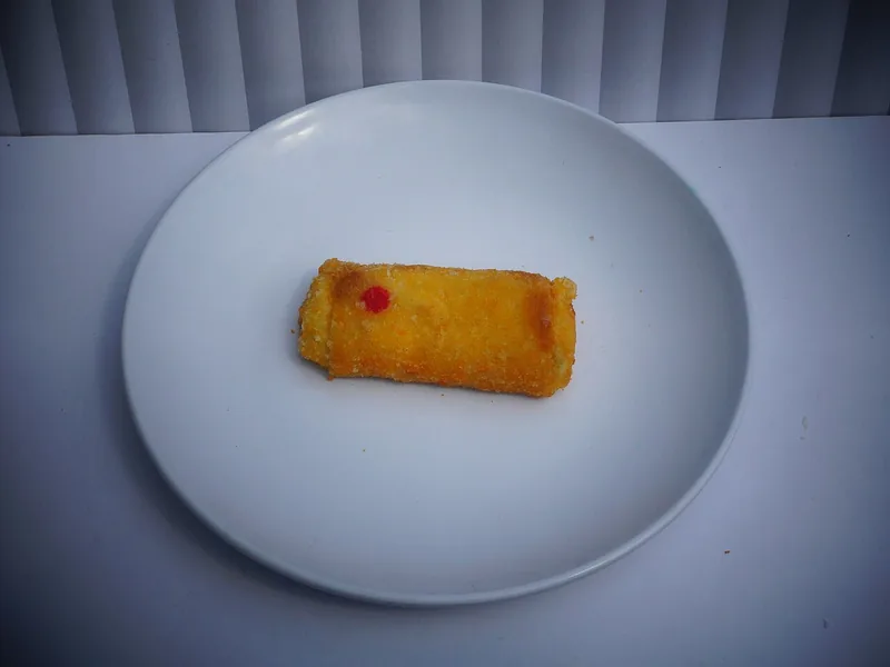 Satu risol goreng berlapis panir kuning keemasan di piring putih