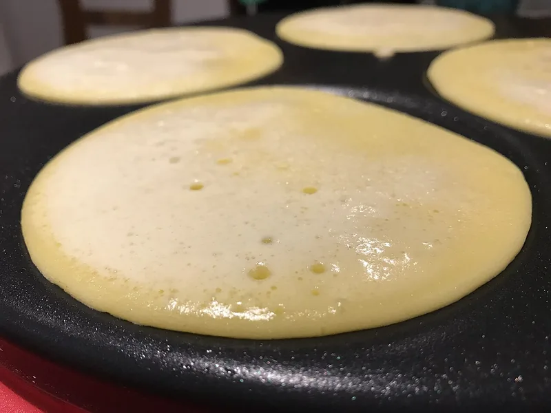 Beberapa lembar kulit dadar tipis sedang dimasak di atas wajan anti lengket berlubang bundar