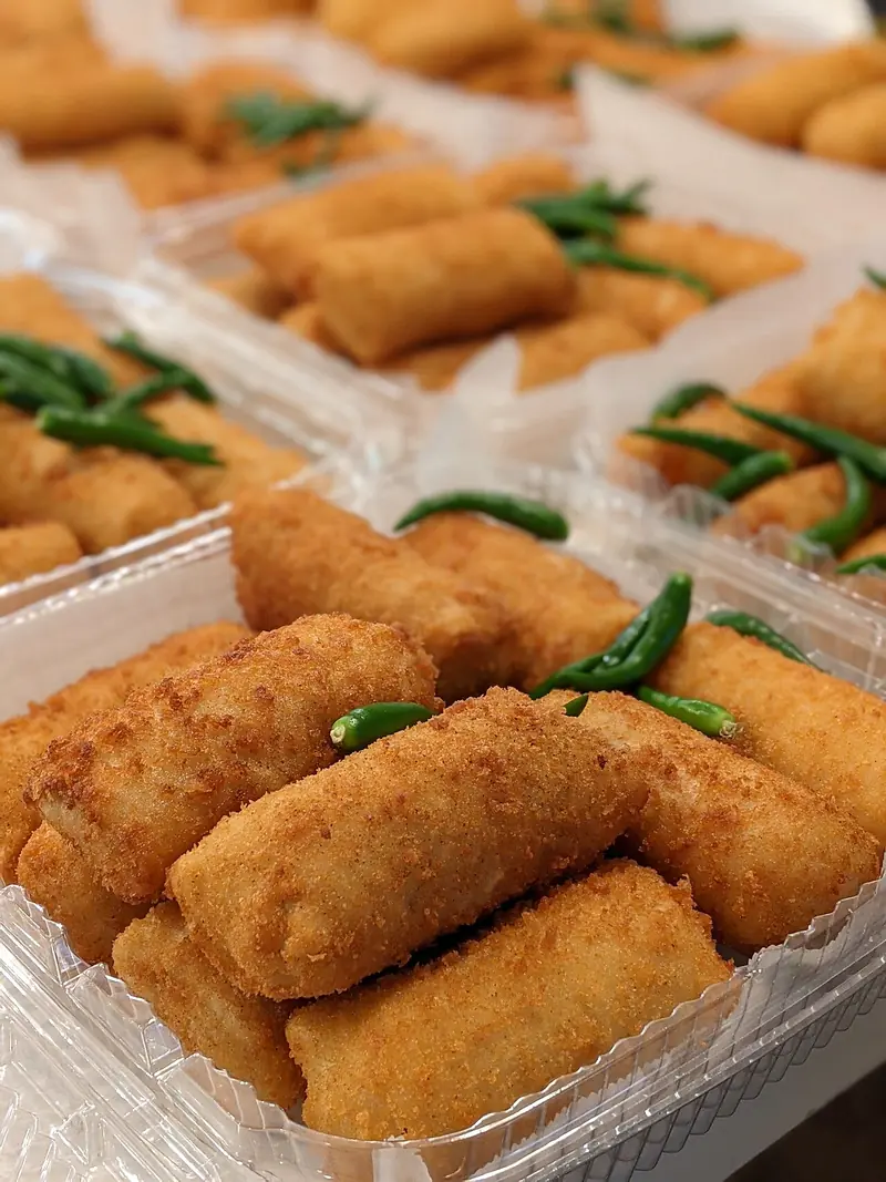 Risol yang baru digoreng berwarna keemasan dikemas dalam mika bersama cabai rawit hijau