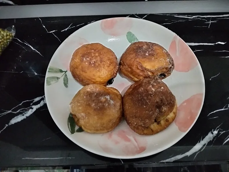 Empat roti goreng bulat isi cokelat bertabur gula di piring bermotif buah