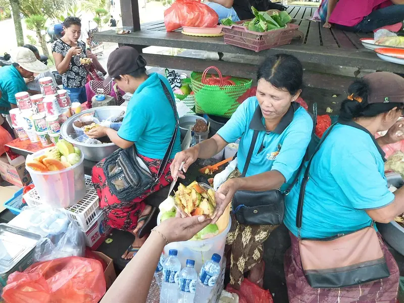 Pedagang perempuan Bali menyiapkan rujak buah dengan mencampur potongan buah dan bumbu di wadah