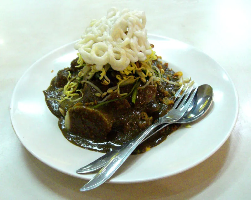 Sepiring rujak cingur berbumbu petis hitam pekat dengan tauge dan kerupuk di atasnya