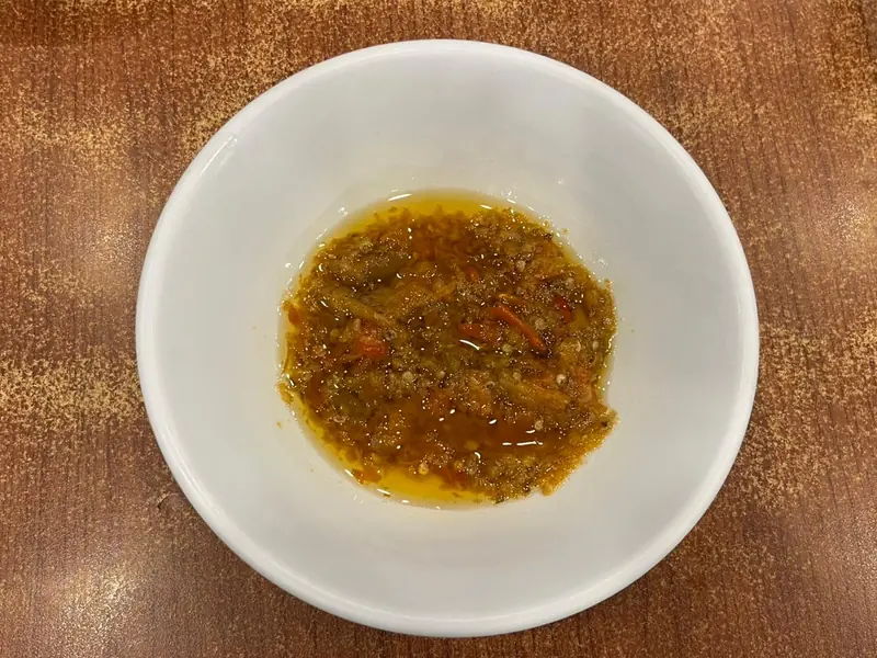 Sambal roa berminyak dengan serat ikan dan potongan cabai di mangkuk putih