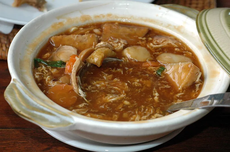 Sapo tahu seafood berkuah merah kecokelatan di dalam pot tanah liat putih bertutup