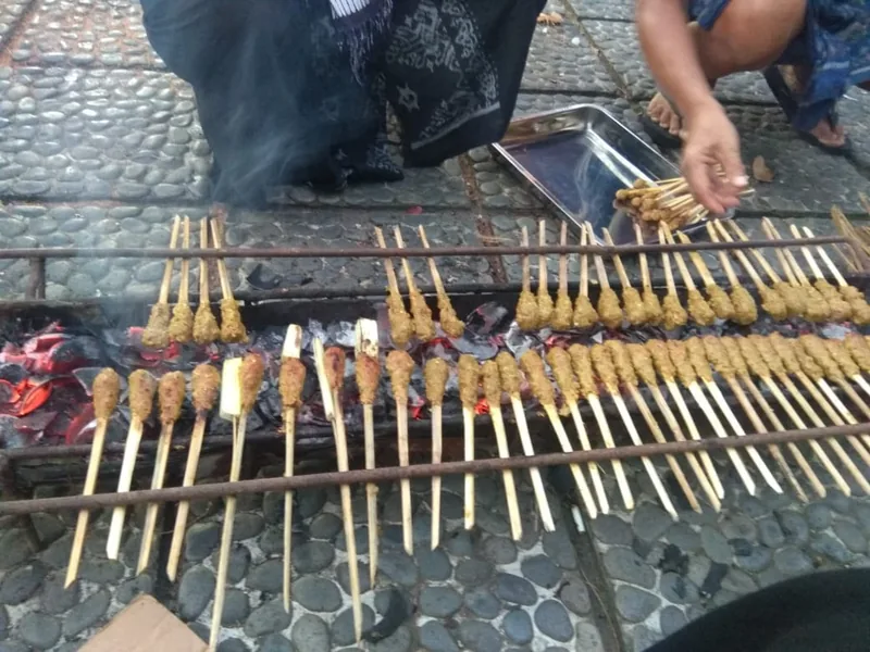 Puluhan tusuk sate lilit dibakar di atas bara arang merah pada panggangan sederhana