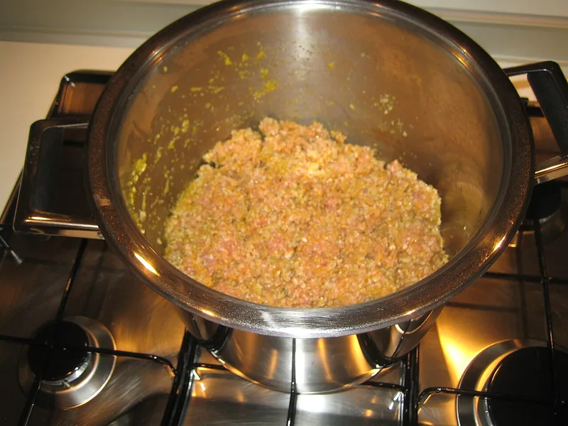 Daging cincang ditumis bersama soffritto di dalam panci stainless di atas kompor gas