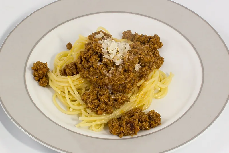 Spaghetti bolognese dengan saus daging cincang cokelat dan serutan keju parmesan di piring putih