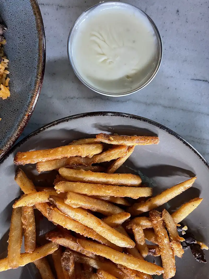 Kentang goreng di piring dengan semangkuk kecil saus keju putih sebagai cocolan