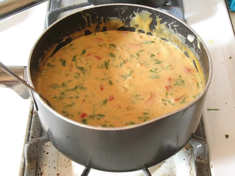 Saus keju kuning oranye yang sedang dimasak dalam panci di atas kompor gas