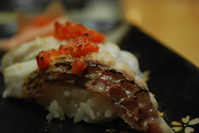 Mentaiko merah jingga di atas sushi ikan putih yang kulitnya dibakar