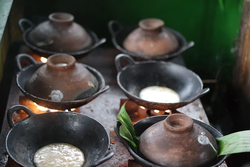 Deretan wajan tanah liat berisi adonan serabi yang dimasak di atas tungku dengan tutup gerabah