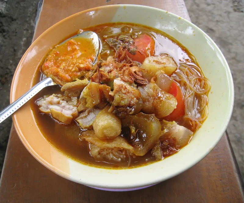 Soto mie Bogor dengan risoles, kikil, bihun, tomat, bawang goreng, dan sesendok sambal di atas bangku kayu