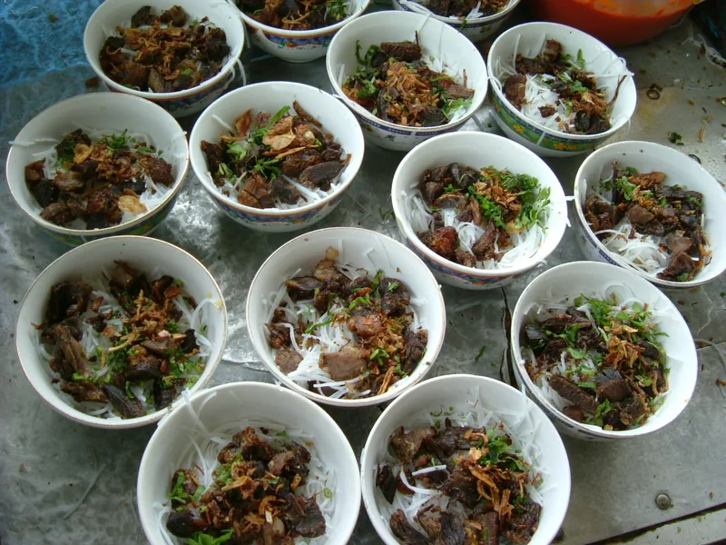 Deretan mangkuk berisi bihun dan irisan daging sapi goreng kering untuk soto Padang sebelum disiram kuah