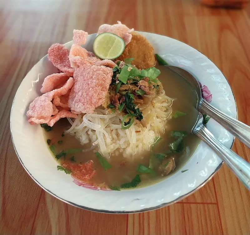Semangkuk soto Padang dengan bihun, perkedel, kerupuk merah, dan jeruk nipis