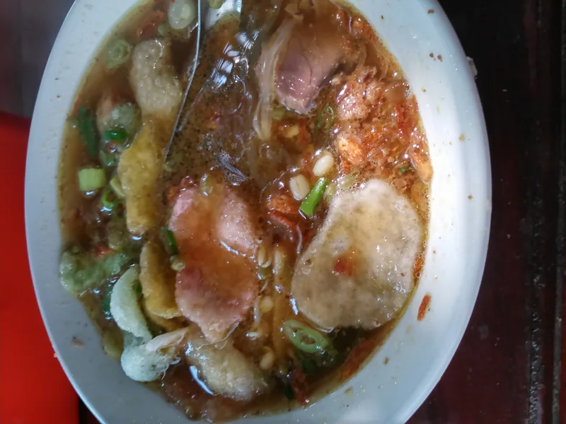 Sroto berisi irisan daging sapi, kerupuk, daun bawang, dan kacang dalam kuah kaldu kecokelatan
