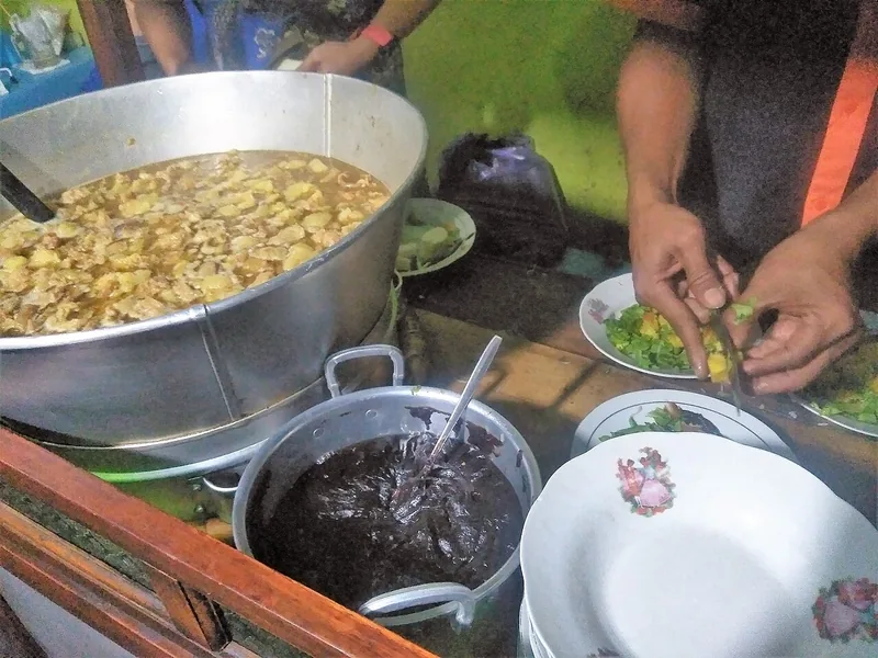 Pedagang meracik tahu campur di samping panci besar kuah kaldu dan panci berisi petis hitam kental