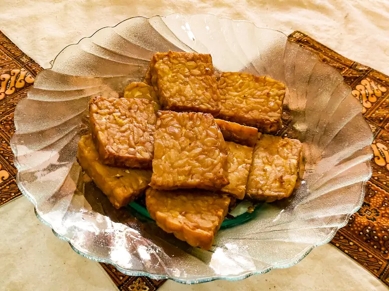 Sepiring potongan tempe goreng kecokelatan dengan butiran kedelai terlihat jelas di piring kaca