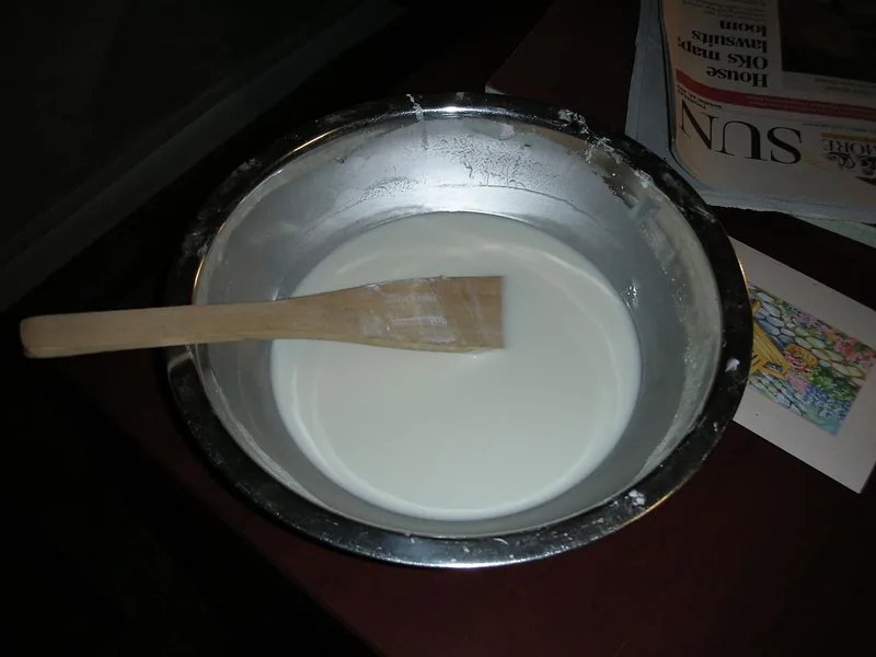 Larutan tepung maizena dan air berwarna putih susu di mangkuk stainless dengan spatula kayu