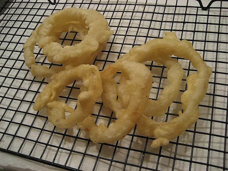 Cincin bawang goreng berlapis adonan di atas rak kawat