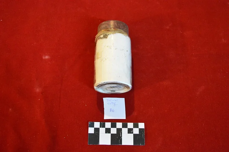 Replika wadah kaca berisi maizena dalam koleksi museum, di atas latar merah