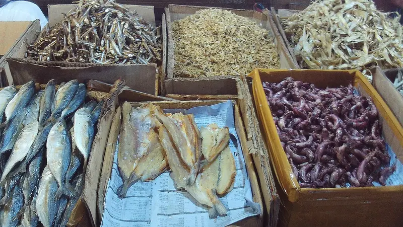 Kardus berisi aneka ikan kering di pasar: teri berbagai ukuran, ikan asin belah, dan cumi kering
