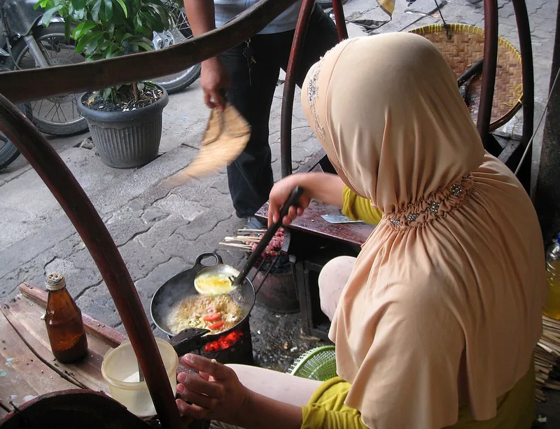 Penjual tongseng memasak kol dan tomat di wajan kecil di atas arang di gerobak kaki lima