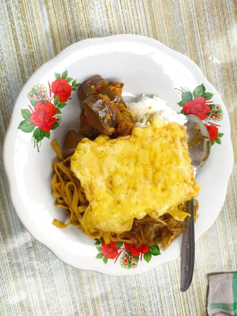 Nasi rames dengan telur dadar, mi goreng, bihun, dan balado terong di piring motif bunga