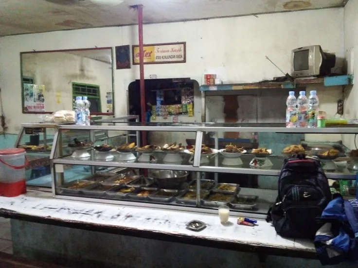 Etalase kaca warung makan berisi piring dan loyang lauk pauk siap dipilih pembeli